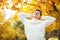 Happy young Caucasian handsome man staying in autumn park, stretching and touching head. Lazy autumn days.