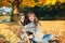 Happy young Caucasian woman sitting on ground hugging dog. Owner walking with pet on autumn fall day. Best friends having fun