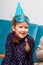 Happy young cheerful little birthday girl in a blue party hat and a carnival mask smiling portrait, twin tails. Kids birthday