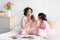 Happy young chinese mom with curlers hold mirror for teen daughter, child apply lipstick on lips sit on bed