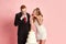 Happy young couple, beautiful woman and man, newlyweds eating cake against pink studio background. Traditions and