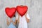 Happy young couple hiding faces behind heart shaped red balloons near grey wall