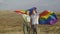 A happy young couple hold hands and raise their hands with a large LGBT flag against the background of hills. A young