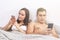 Happy young couple lying in bed and using smartphones. Online shopping, video chatting