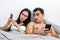 Happy young couple lying in bed and using smartphones. Online shopping, video chatting