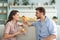 Happy young couple in pajamas in kitchen having breakfast, feeding each other a croissant