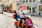 Happy young couple riding a scooter in the city on a sunny day. Handsome man in glasses rides a moped, while his