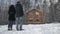 Happy young couple standing near wooden cottage. Stock. Couple stands near the house in the forest in winter