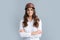 Happy young cross-armed female engineer in helmet and hardhat on grey background.