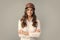 Happy young cross-armed female engineer in helmet and hardhat on grey background.