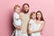 Happy young family with adoravle little daughters posing on pink background