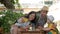 Happy young family with a baby eating on the open air in a cafe. Everyone is sitting on small wooden chairs