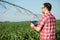 Happy young farmer or agronomist controlling large irrigation system with a tablet