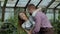 Happy young florist couple in apron have fun while working in greenhouse. Laughing woman spray water in husband face and