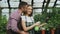 Happy young florist family in apron working in greenhouse. Attractive man embrace and kiss his wife while she watering