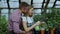 Happy young florist family in apron working in greenhouse. Attractive man embrace and kiss his wife while she watering