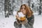 A happy young girl blows on the white snow, which lies on cozy knitted woolen mustard-colored mittens. Blurred snowflakes in the