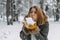 A happy young girl blows on the white snow, which lies on cozy knitted woolen mustard-colored mittens. Blurred snowflakes in the