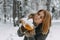 A happy young girl blows on the white snow, which lies on cozy knitted woolen mustard-colored mittens. Blurred snowflakes in the