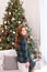 Happy Young girl in dress sit on sofa in Christmas living room. Smiling little girl near christmas tree at home. Merry Christmas a