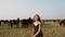 Happy young girl on the field with grazing horse herd at summer