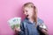 Happy young girl with silver piggy bank and euro banknotes  on pink background. save money concept.