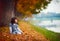 Happy young girl sitting in fallen leaves in autumn park