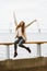 Happy young girl sitting on waterfront at pier in the port, enjoying life and waving his arms. Woman with long hair smiles and