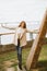 Happy young girl standing on waterfront at pier in port, enjoying life and waving his arms. Woman with long hair smiles and enjoys