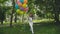 Happy young girl walks in the green sunny park and holds colourful balloons