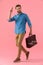 Happy young guy in denim shirt holding suitcase and military saluting