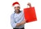 Happy young handsome man wearing santa hat holding red shopping bag