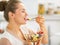 Happy young housewife eating fresh fruit salad in kitchen