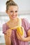 Happy young housewife peeling banana in kitchen