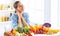 Happy young housewife sitting in the kitchen preparing food from a pile of diverse fresh organic fruits and vegetables