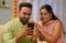 Happy young Indian couple using mobile phone together at home during diwali festival celebration in front of gifts-