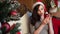 Happy young lady in Christmas costume playing with multicolored balls hanging in the room with decorated New Year