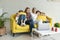 Happy young lesbian couple with daughters in casual clothes sitting together on yellow sofa at home, exited family