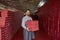 Happy young male worker standing in shoe warehouse and holding boxes of new footwear