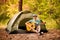 Happy young man camping and strum a guitar instrumental music to relax against background of forest sunset.