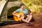 Happy young man camping and strum a guitar instrumental music to relax against background of forest sunset.