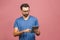 Happy young man in casual standing and using tablet over pink background