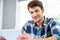 Happy young man in checkered shirt using tablet at home