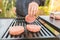 A happy young man cooking meat burgers on barbecue grill - leisure, food, people and holidays concept