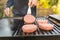 A happy young man cooking meat burgers on barbecue grill - leisure, food, people and holidays concept