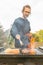 A happy young man cooking meat burgers on barbecue grill - leisure, food, people and holidays concept