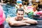 happy young man looking at camera near poolside while his female friends resting on inflatable mattresses