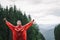 Happy young man in red raincoat on a mountain hike enjoys the freshness rain with a smile on his face and hands raised up.Mountain