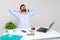 Happy young man sitting at table in office and stretching himself