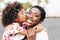 Happy young mother having fun with her child in summer day - Daughter kissing her mum outdoor - Family lifestyle, motherhood, love